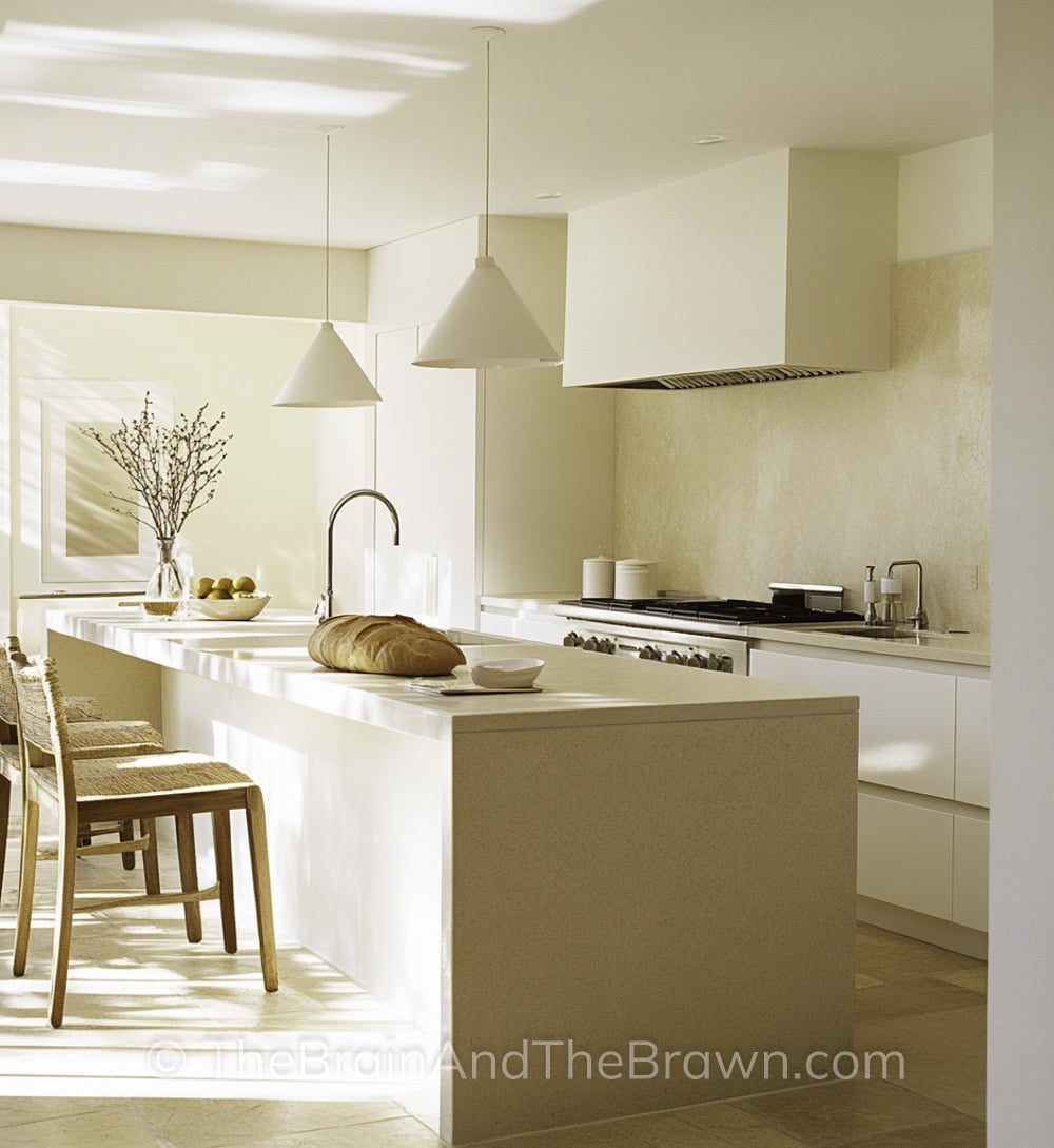 modern, clean minimalist kitchen with cream and beige paint colors on island, stove hood, pendants, backsplash, drawers and backsplash. Woven barstools at island.