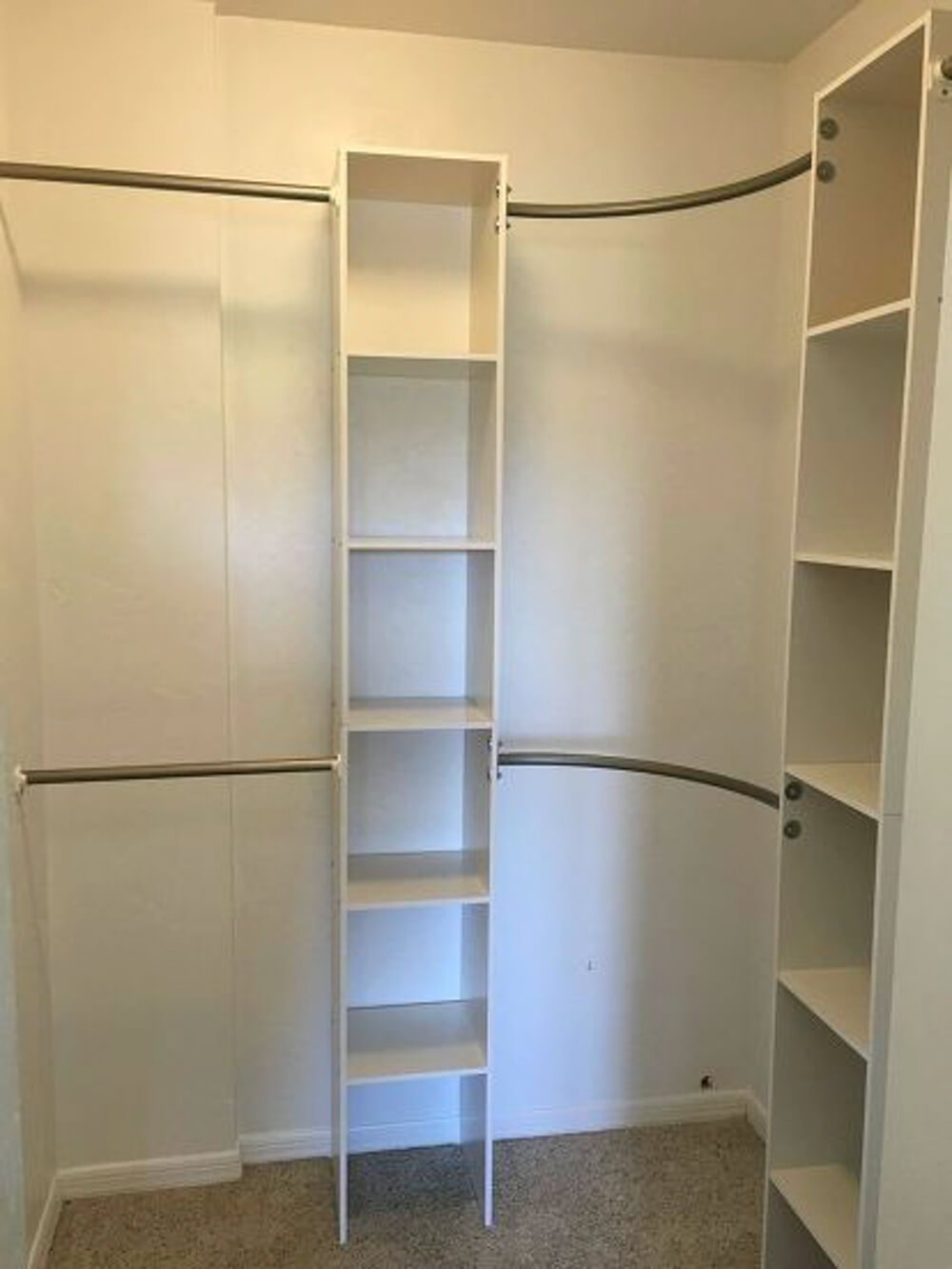 small walk in closet with white shelves and hanging rods curved in corner