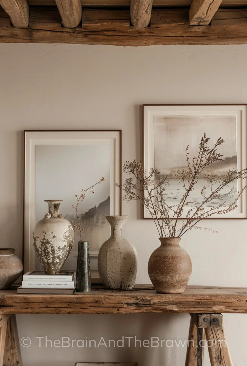 A beautiful rustic wooden ceiling with beams provides modern farmhouse ideas in this entry way that also has a rustic wooden console table with neutral landscape art that hangs above the console table with ceramic vases that sit on the console table. 