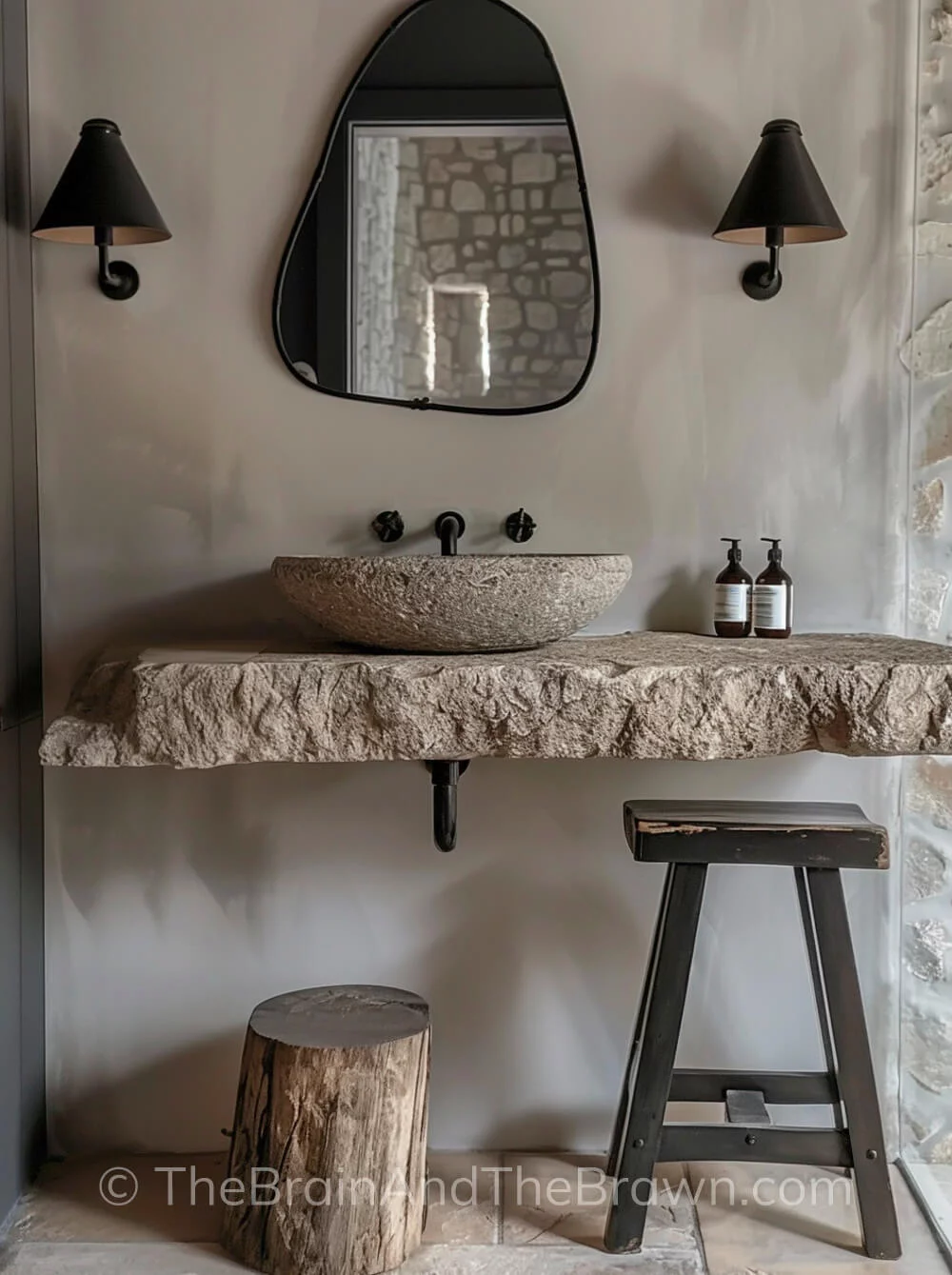 Modern farmhouse ideas in a bathroom with a stone vessel sink on top of a wall mounted stone slab. A rustic counter stool and wood stump set below the wall mounted sink. A black non-symmetrical mirror and black wall sconces are mounted on the wall above the sink. 