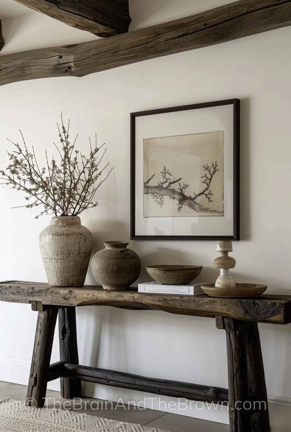 Modern farmhouse interior ideas with a long wooden console table against a white wall. A piece of neutral artwork hangs above the console table and a console table has a vignette of pottery on top of it. 