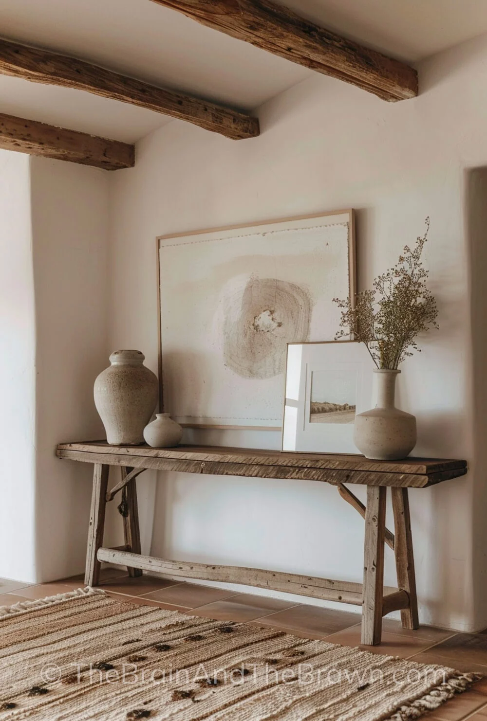 An entry way showing modern farmhouse ideas with a rustic wooden console table and large art hangs on white walls with a neutral textured rug in front of the console table.