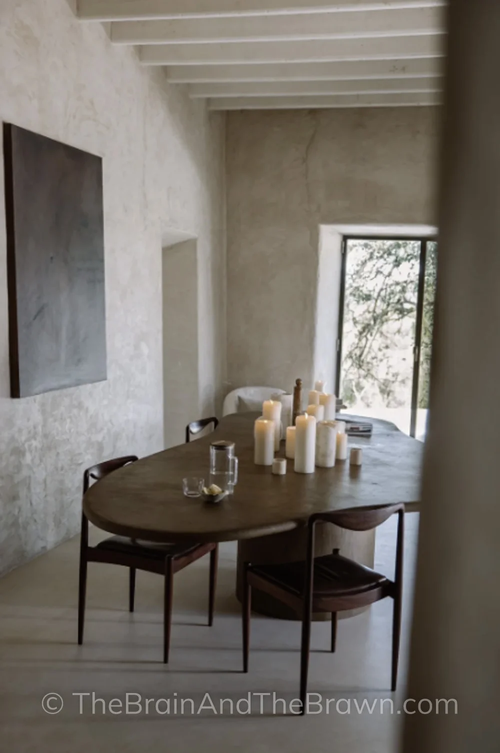 Dining room idea with plaster walls, dark plaster dining table, wooden chairs and lots of candles on top of the dining table. 