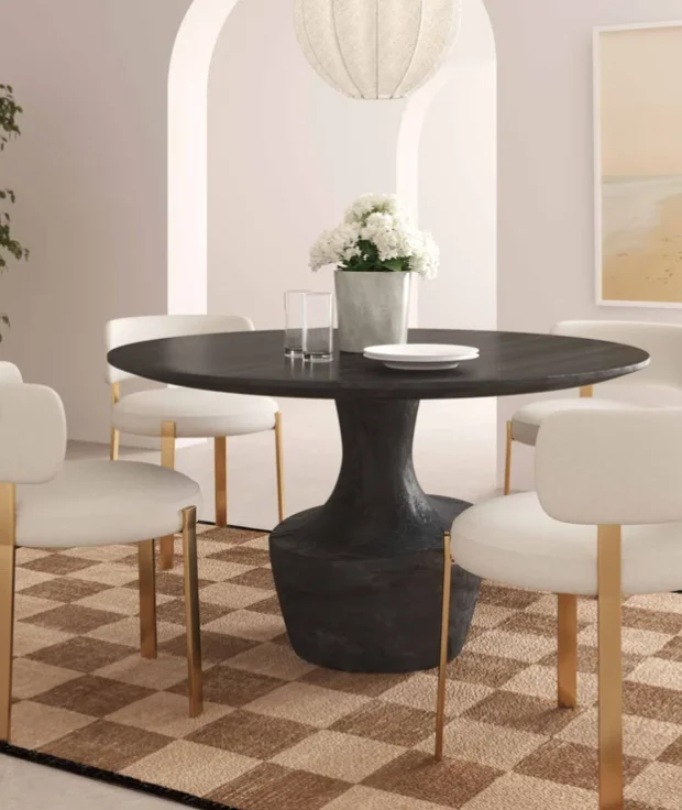 A dining room idea with a round, plaster dining table, white upholstered chairs and a neutral checkered rug. 