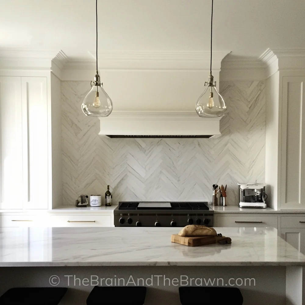 An off-white kitchen with a chevron tile backsplash behind the stove and white quartz countertops