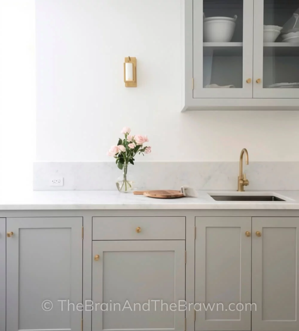 Grey kitchen cabinets, brass hardware, marble countertops with low marble backsplash that matches the countertops