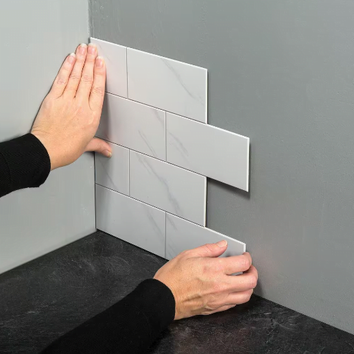 A person installs white subway tile peel and stick backsplash