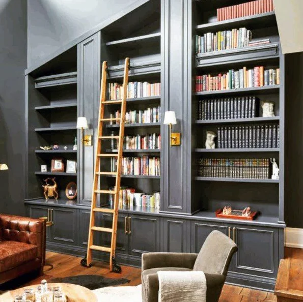 Dark painted floor to ceiling bookshelves with ladder and brass pendant lighting