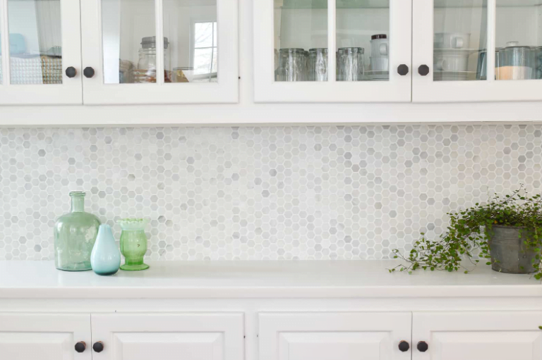 Small white kitchen backsplash idea with penny tile, white cabinets, black hardware, and white quartz countertop