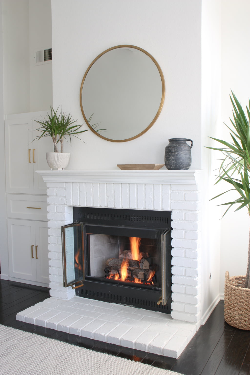 A white painted fireplace with round brass mirror above it.