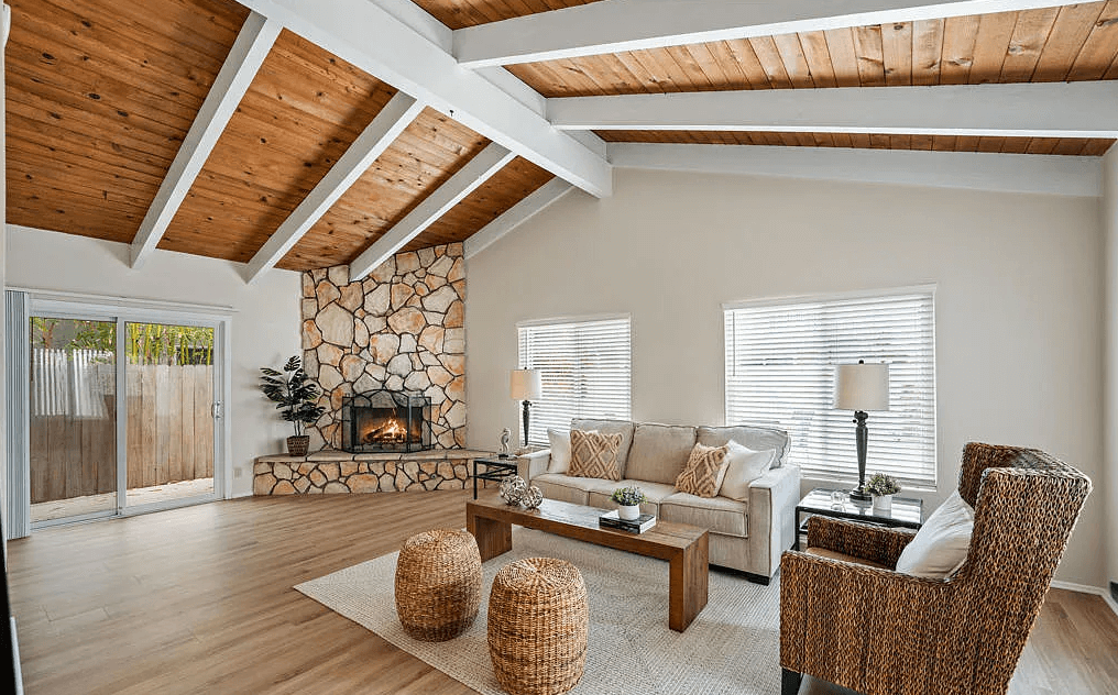 A large awkward living room layout with corner fireplace and exterior doors. A couch and one chair sit in front of the windows.