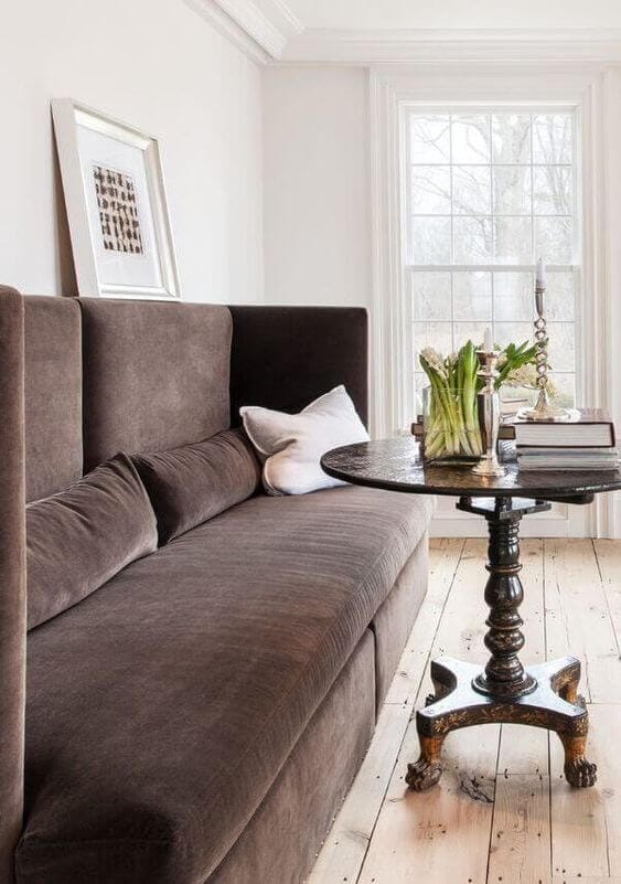 Brown upholstered banquette seat with a small round wooden table in front of it