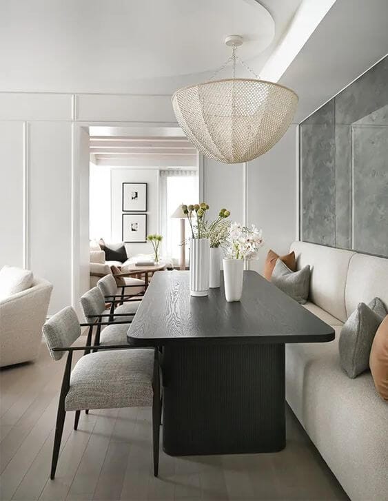 A dining space with a wooden rectangular table, upholstered dining chairs on one side of the table and a cream upholstered banquette bench on the other side of the table