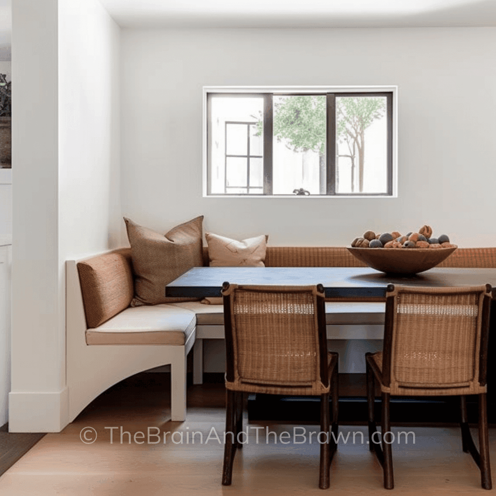 Dining room with banquette seating along two sides of a wooden rectangular table and two cane chairs on the other side  