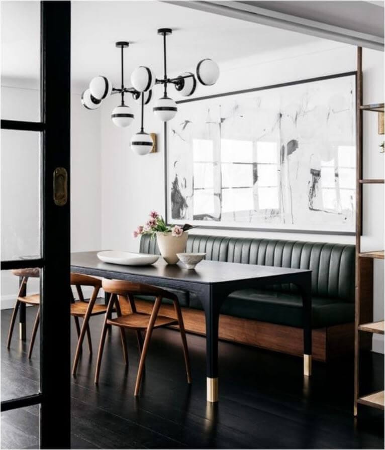 Dining room with a black leather and wooden dining bench against one wall, a large piece of art hangs above the bench with a black rectangular table and three wooden dining chairs opposite the bench