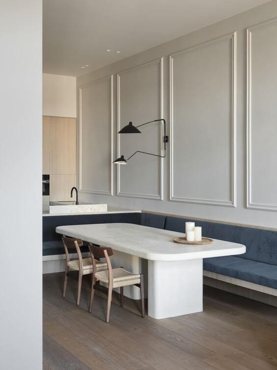 A dining area with stone dining table and a custom blue velvet upholstered l-shaped banquette seating around the table