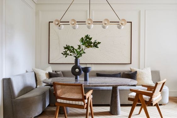 Dining room with a large upholstered l-shape banquette bench, an oval stone dining table and two wooden dining tables