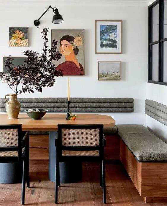 Dining room with channeled banquette back cushion still mounted right to the wall, oval wooden dining table and gallery wall above the bench