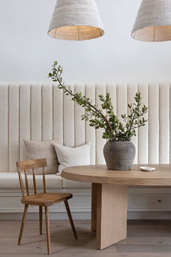 Custom banquette seat with a tall upholstered back in a boucle fabric with an oval wooden dining table in front of the bench