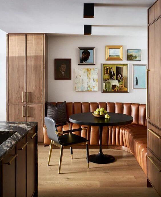 A curved leather banquette bench with a black tulip table. A gallery wall of art hangs above the bench.