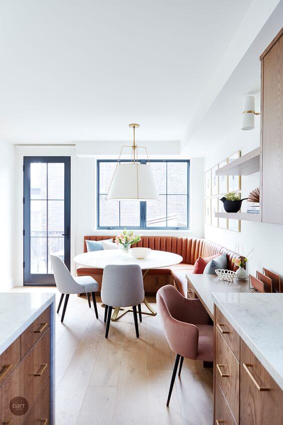 An eat in kitchen with a round dining table, two upholstered dining chairs and a custom curved leather banquette bench along two walls