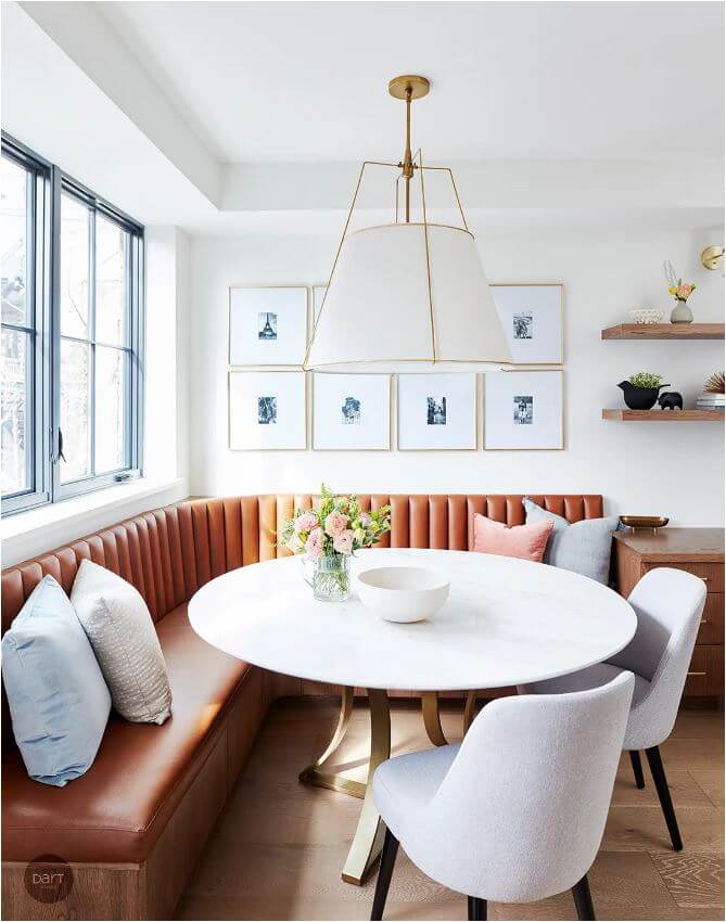 A dining room with a white round table, two upholstered chairs and a leather l-shaped banquette seat