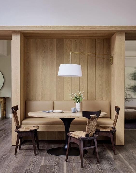 A dining nook with a tulip table and a custom built in wooden bench with leather upholstery and vertical wooden paneling above the bench