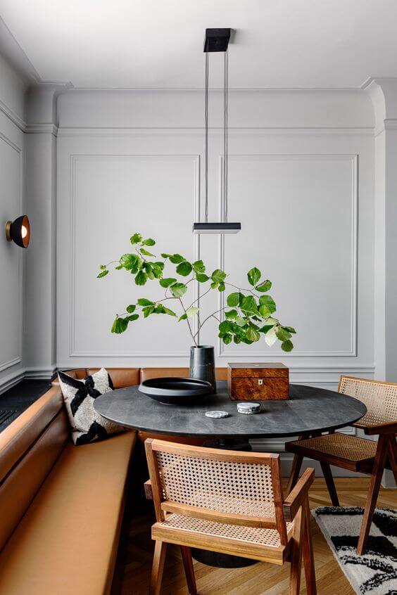 Leather banquette seat with a black round table in front of it and two wooden and cane chairs on the other side of it. 