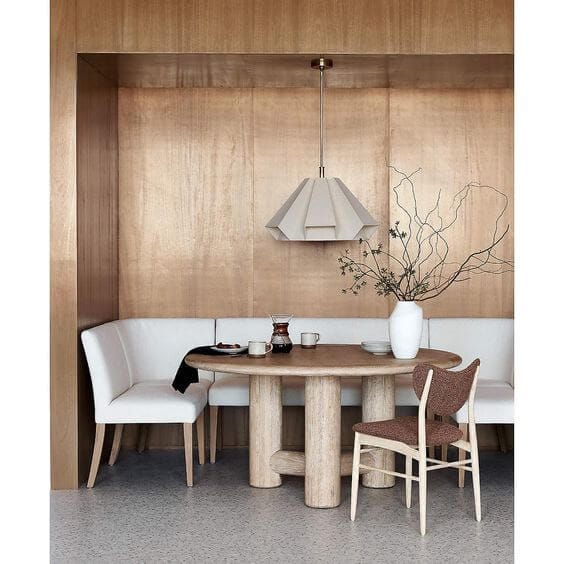 A dining space with a wooden round dining table and an upholstered dining bench with wooden legs