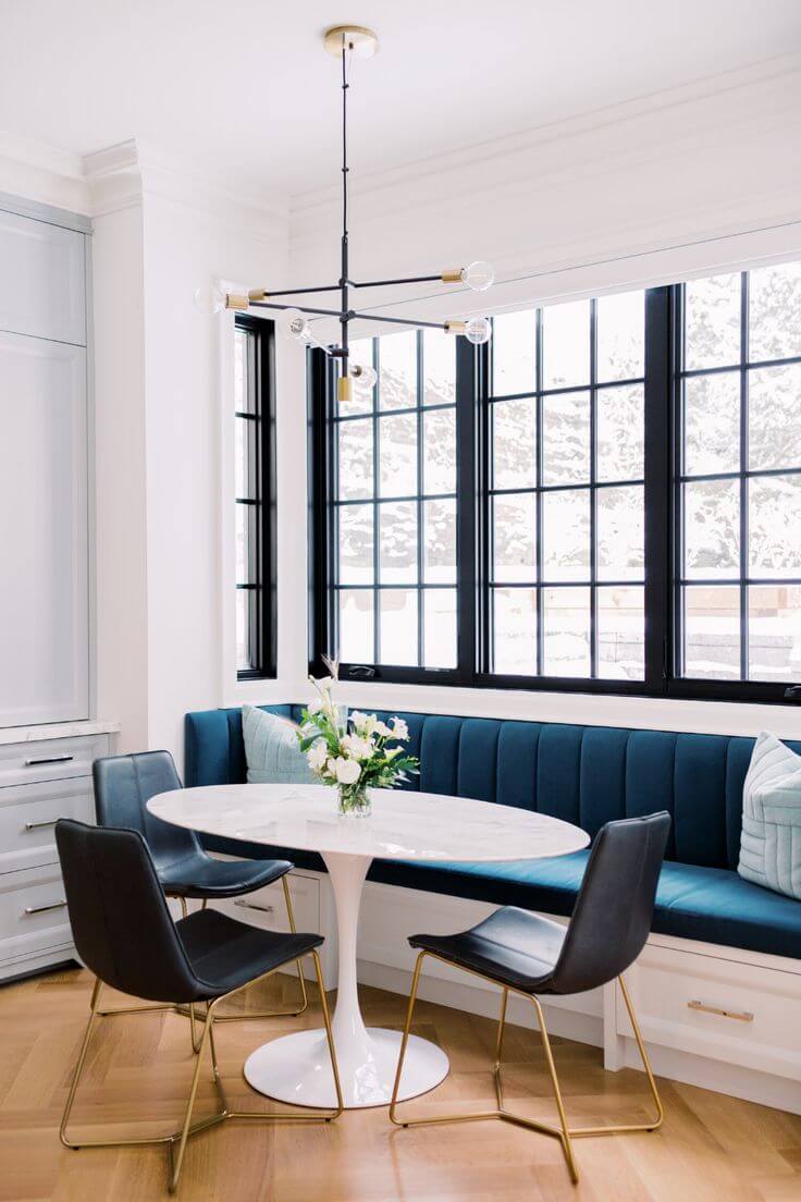 A dining space with a banquette seat in front of a window with a white tulip table in front of the bench and three leather chairs around the table.