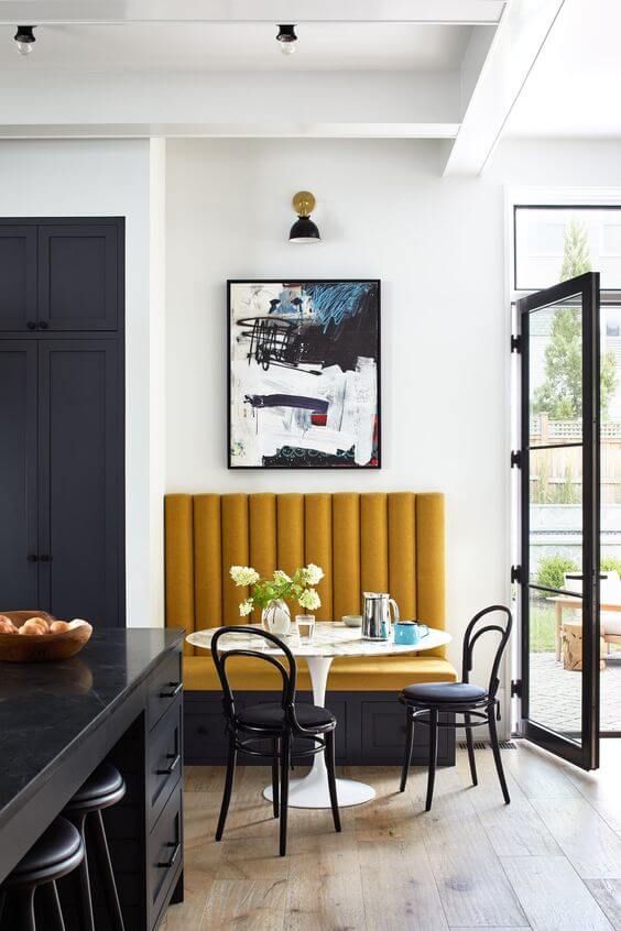 A small banquette bench with a white tulip table and two black bistro chairs. 