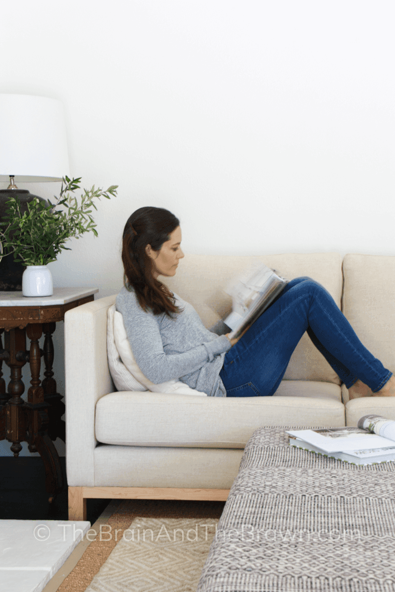 A woman sits on a couch reading a magazine in her home