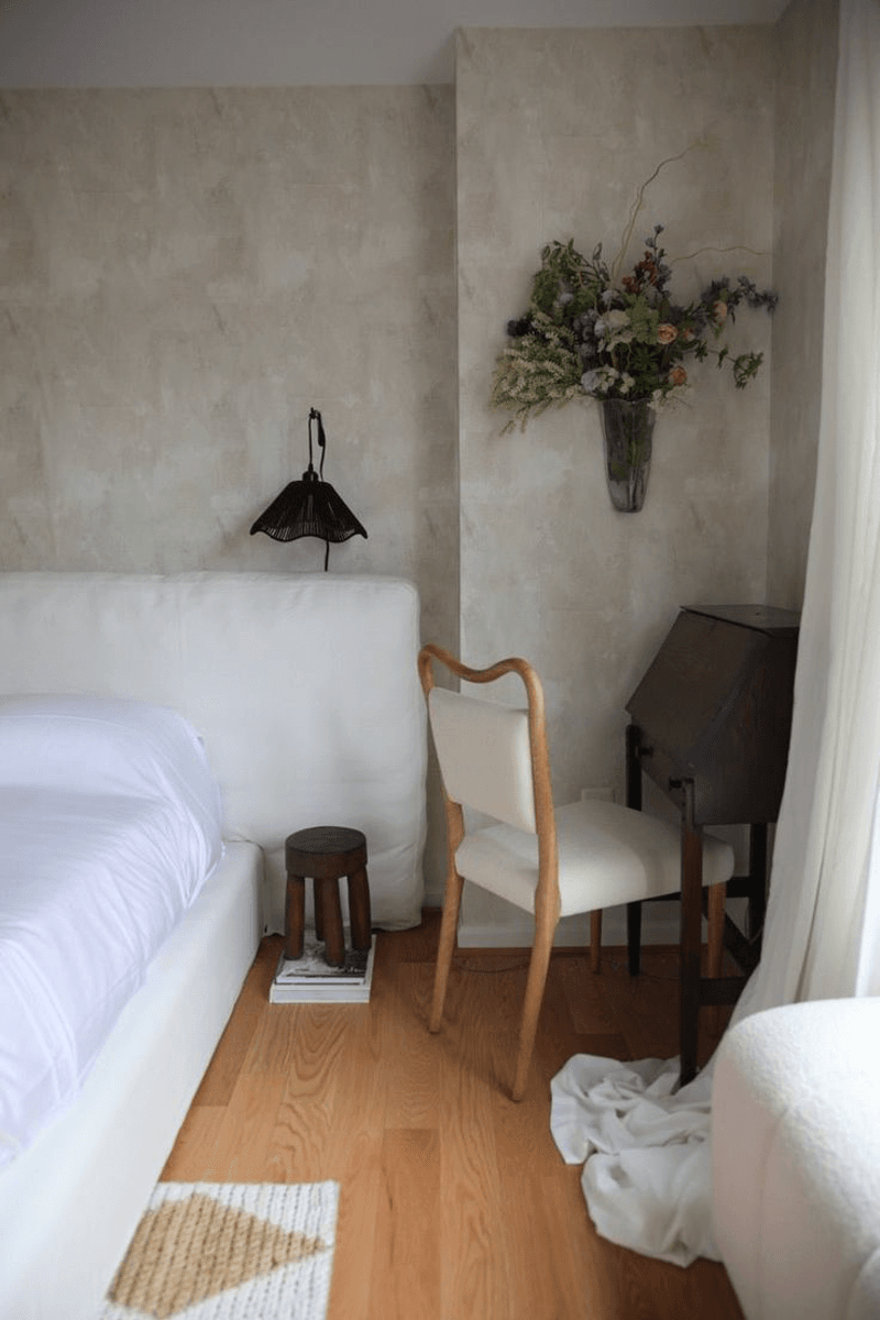 Bedroom with a textured tan wall and a black wicker wall sconce. Dried florals are also hung on the textured wall