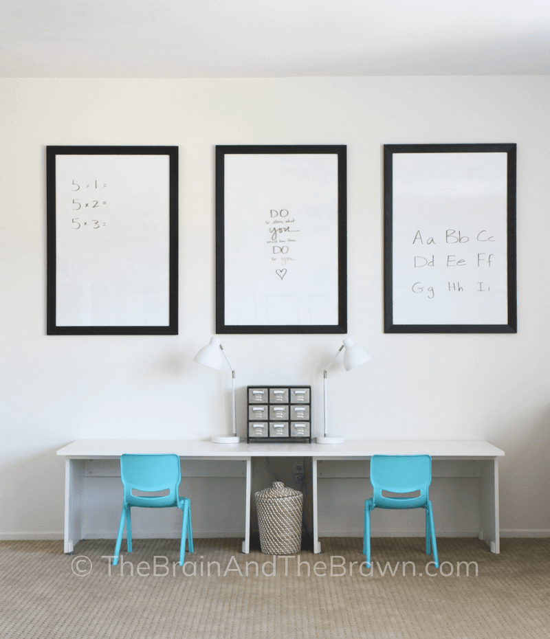 Playroom with one long child size desk and two chairs. Three picture frames hang above the desk and are used as dry erase boards