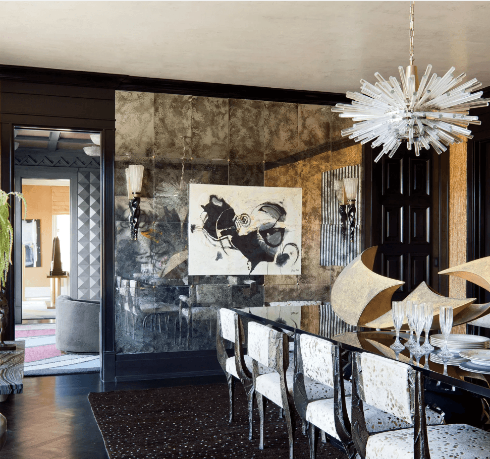 A moody dining room wall decor idea with floor to ceiling antique mirrors along one wall of the dining room. Hanging on top of the antique mirror wall are two wall sconces with a large abstract piece of art hanging in the middle 