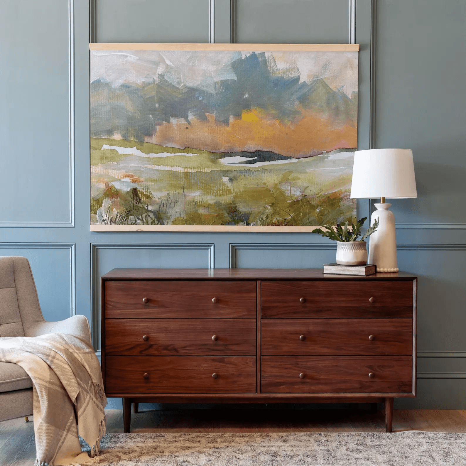 Office wall art idea of a landscape tapestry hanging on a light blue wall with walnut dresser below it