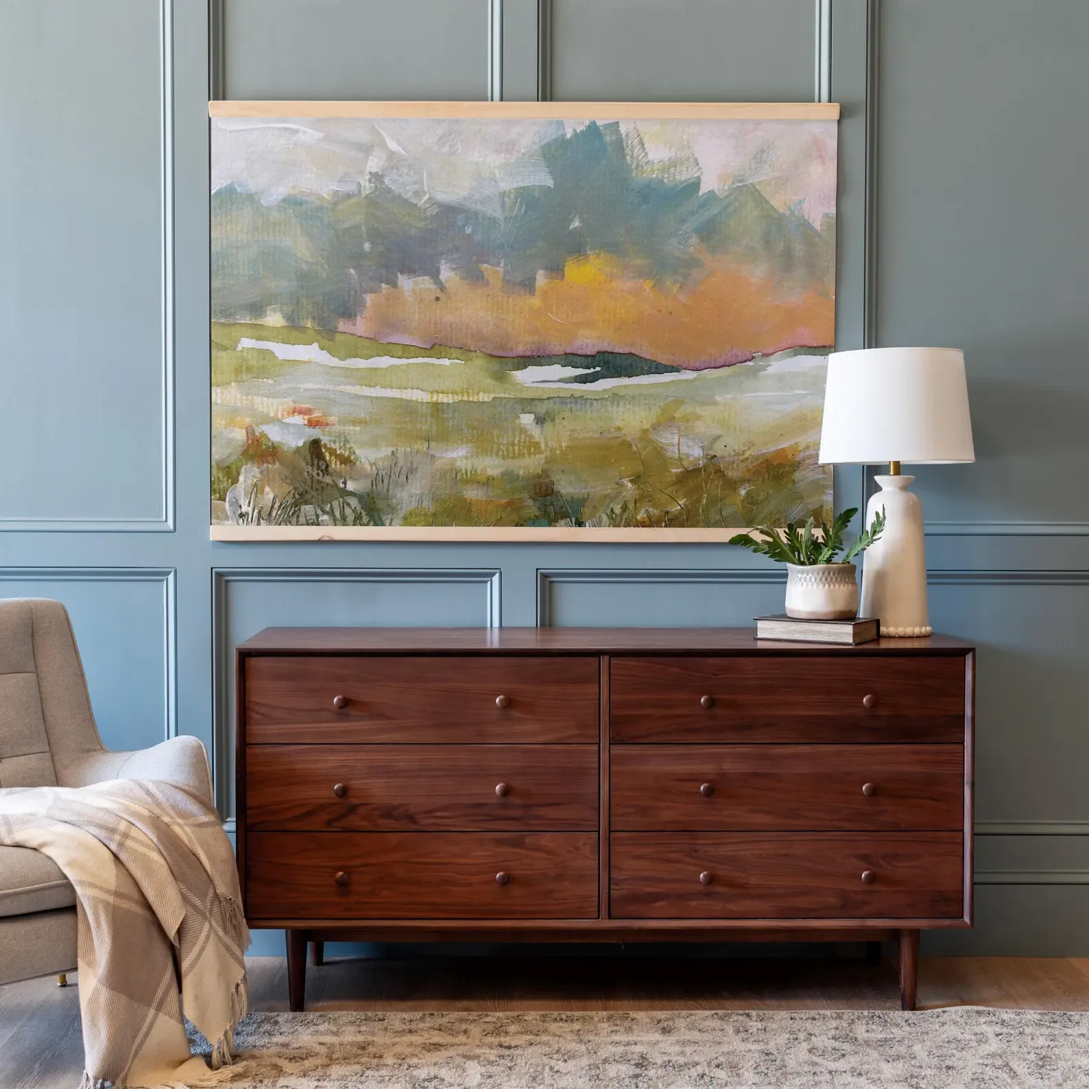Office wall art idea of a landscape tapestry hanging on a light blue wall with walnut dresser below it
