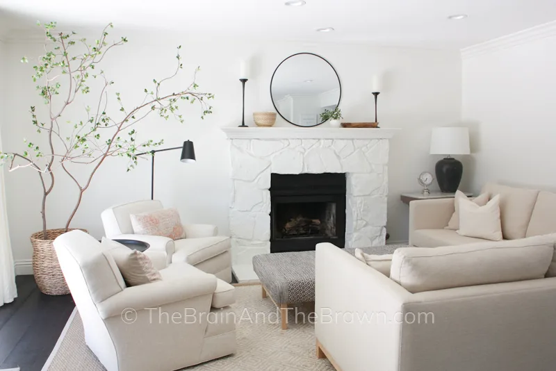 A full view of a fireplace in a living room with two neutral chairs and a neutral l-shaped sectional