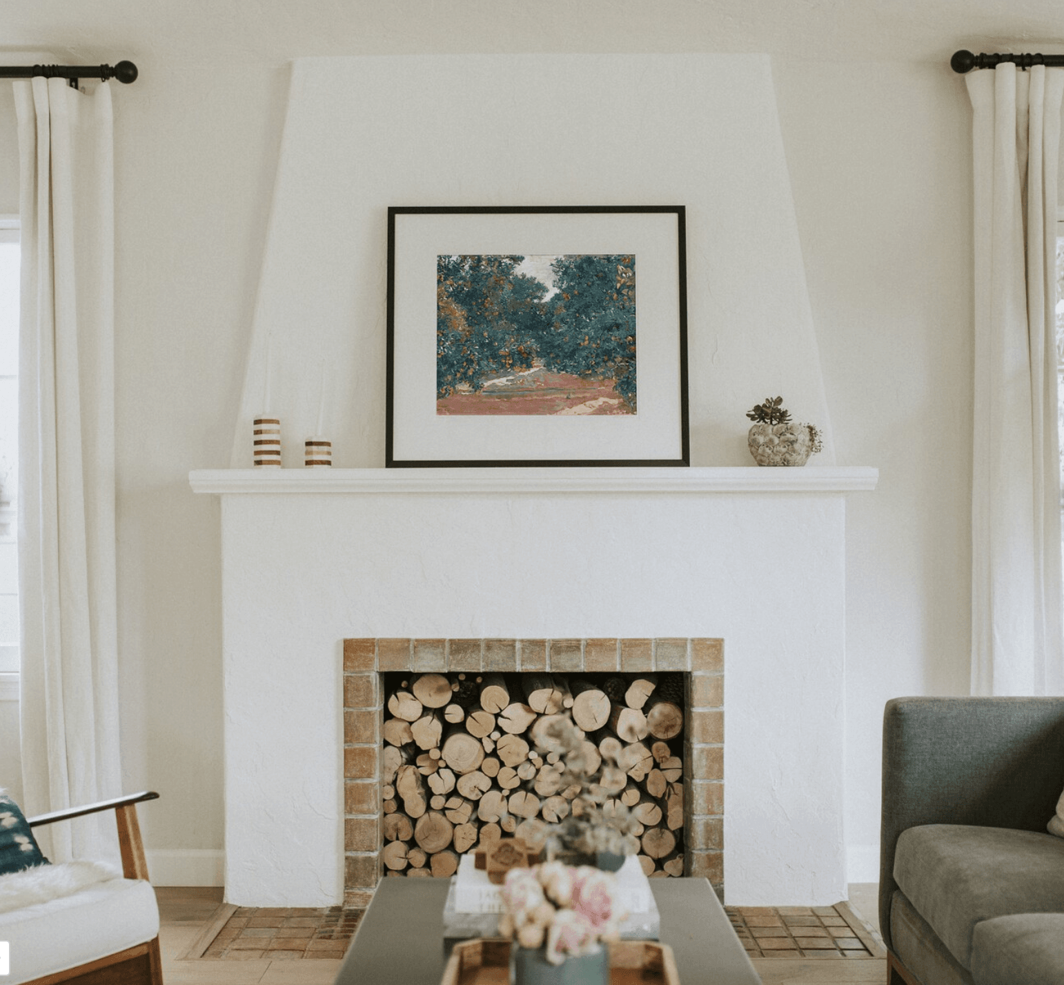 A white plaster fireplace in a living room with a piece of Spanish artwork on the mantel 