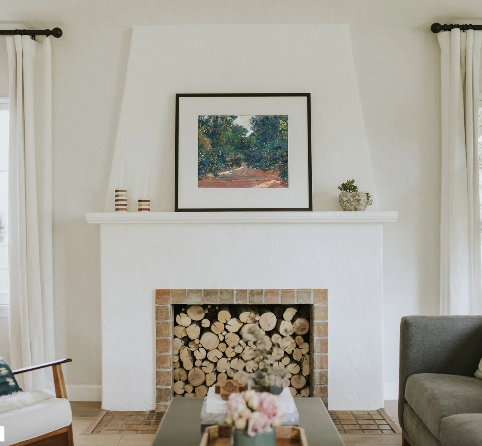 A white plaster fireplace in a living room with a piece of Spanish artwork on the mantel 
