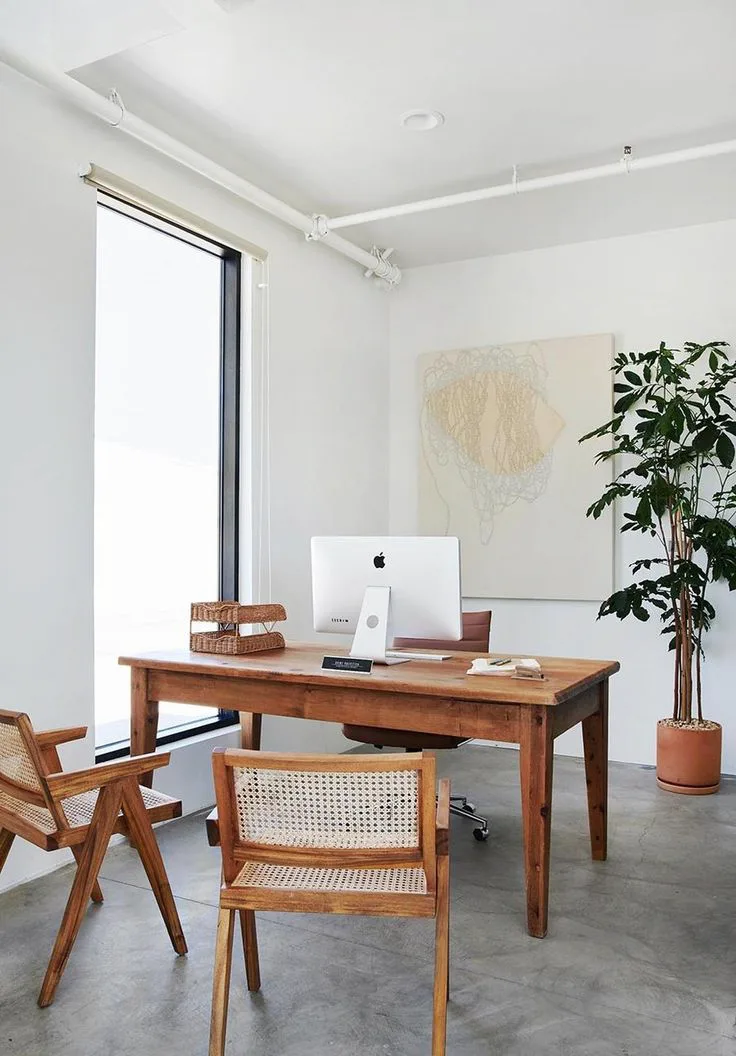 simple beach-style home office with concrete floors, wood desk and chairs, plant and modern artwork on wall