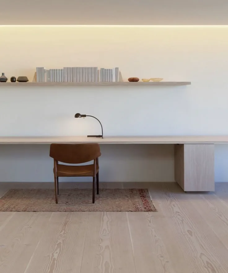 a minimalist home office with simple natural wood desk and floating shelf above, and light wood floors
