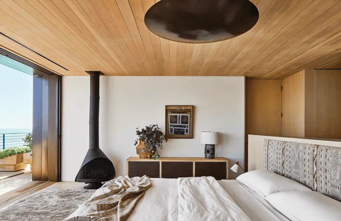 a beach house bedroom in mid-century modern style with wood paneling on ceiling and fireplace in bedroom