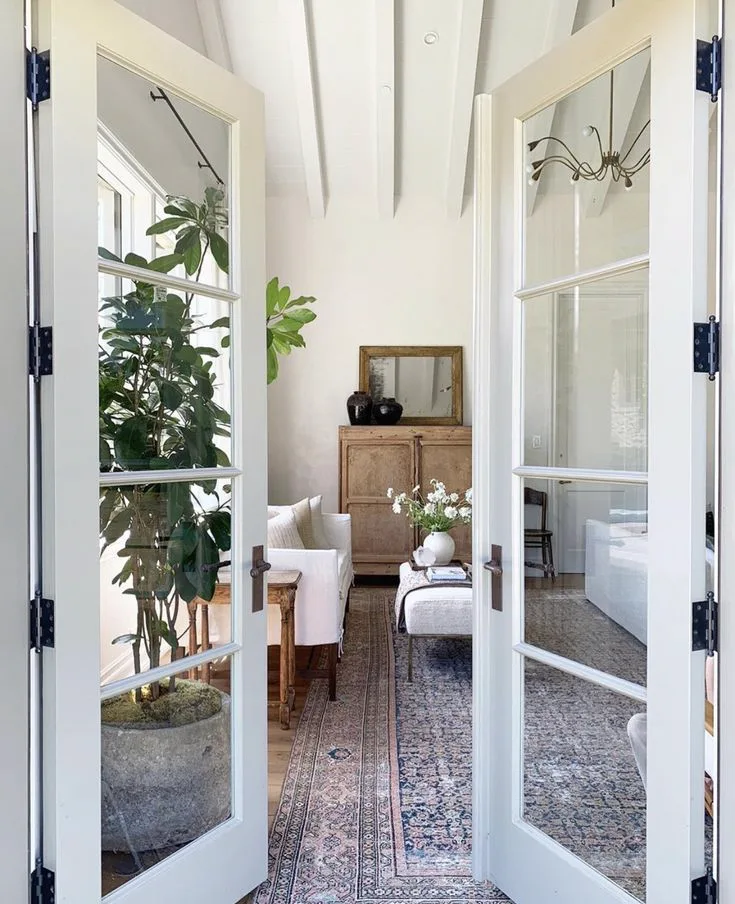 white French doors opening to a living room interior with rug and bright white colors in modern transitional style