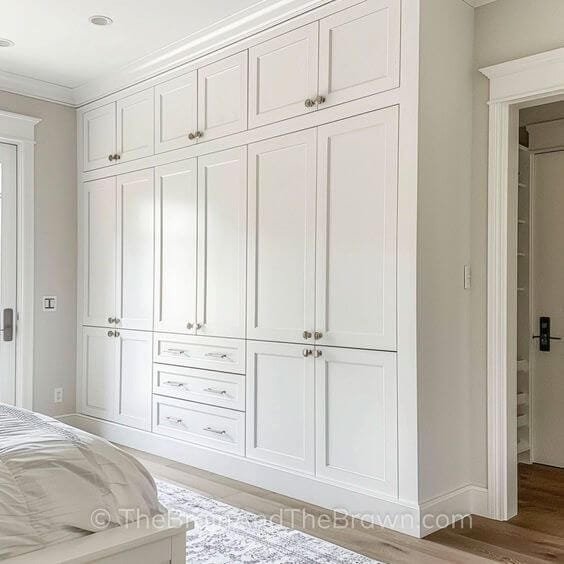 a creamy white built in closet with mostly cabinets and three drawers, silver hardware