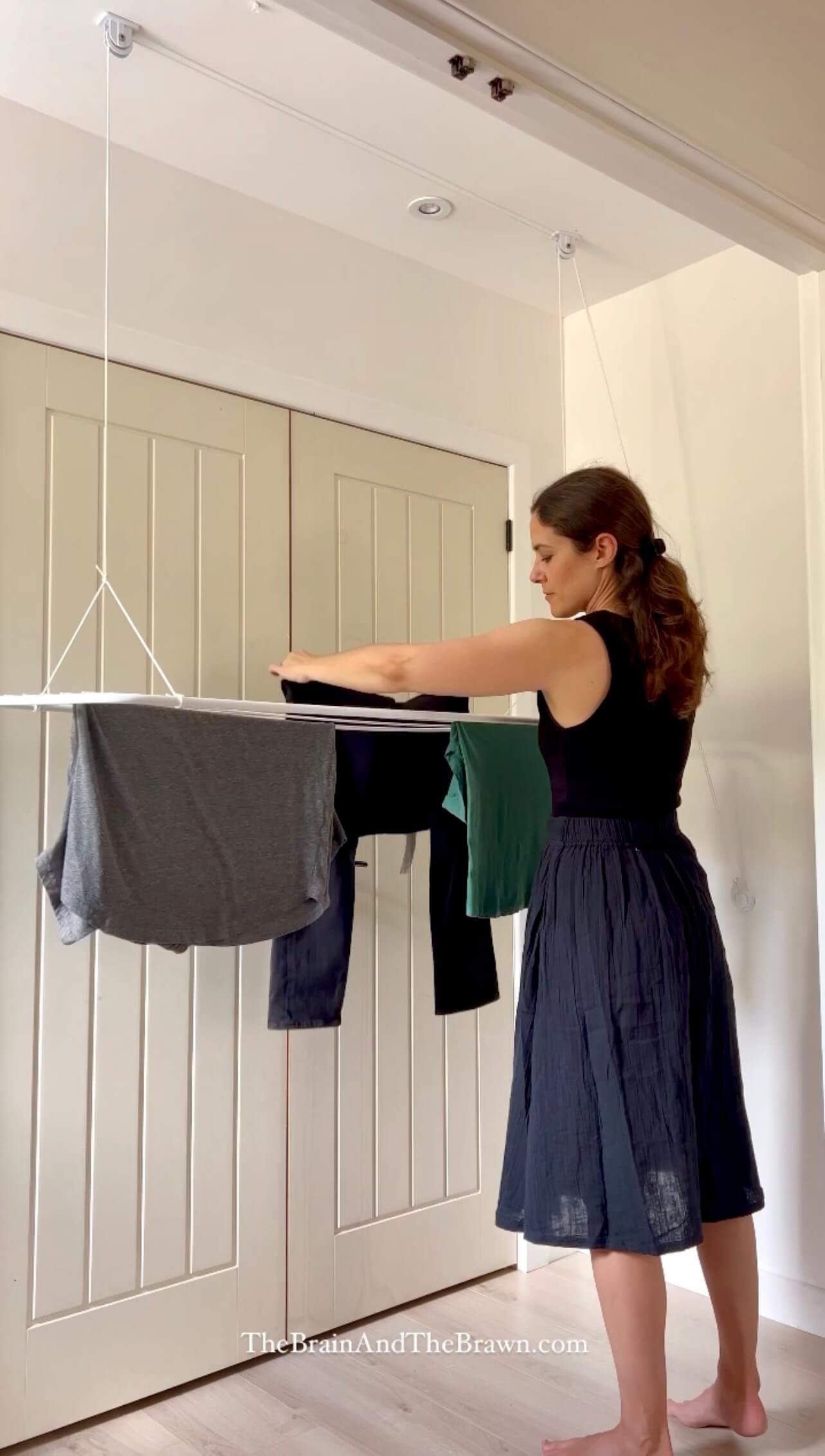 a woman hanging on a ceiling drying rack in a laundry room