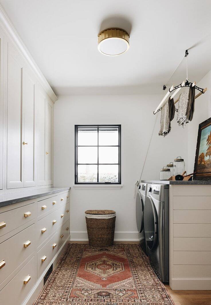 a grey and beige laundry room with drawers and cabinets, gold hardware
