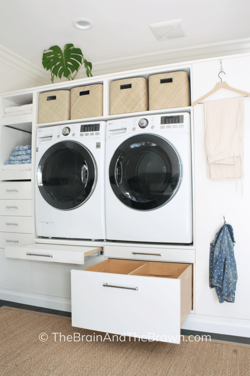 a white laundry cabinet design with raised washer and dryer in a one-wall laundry room 