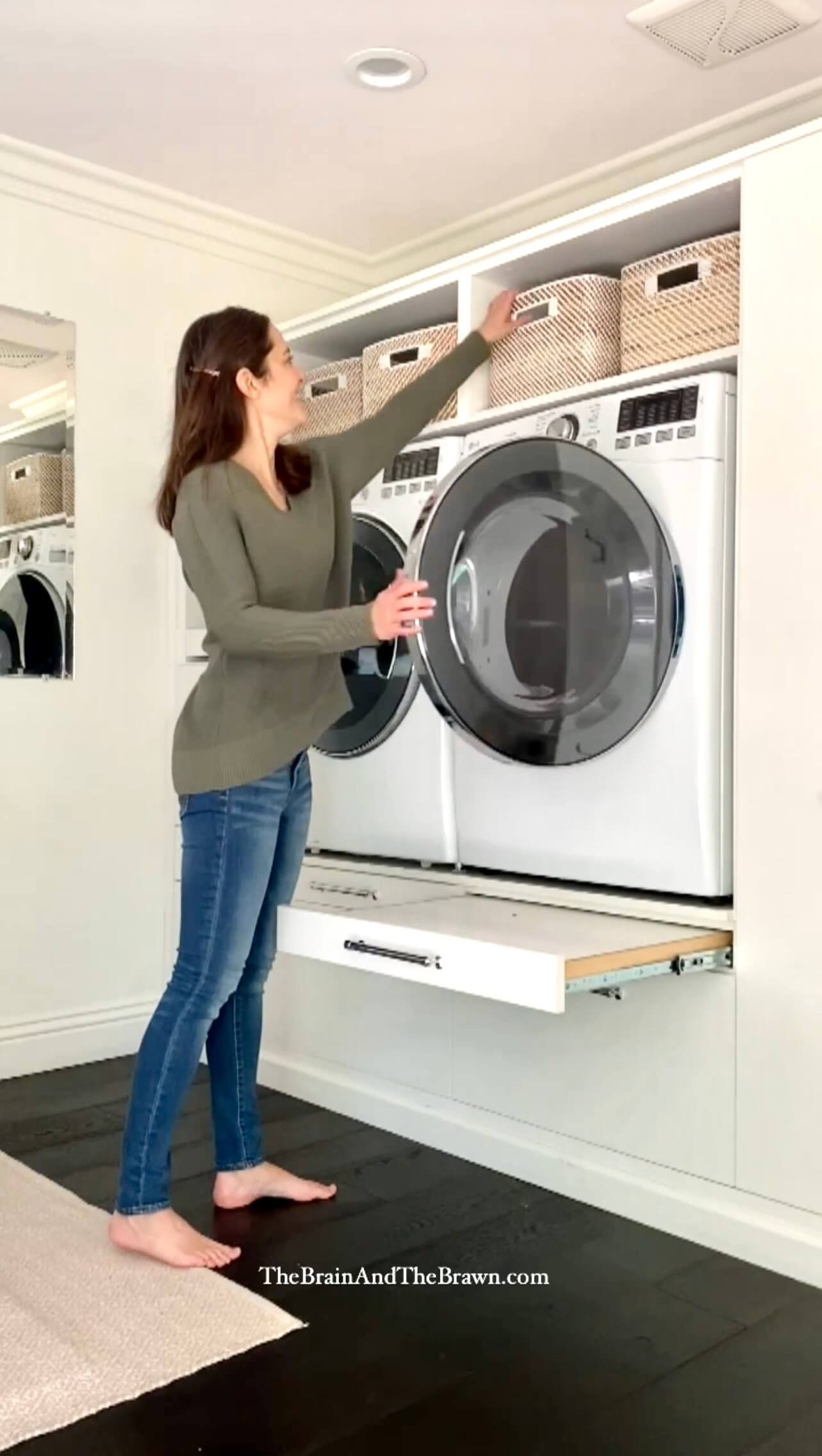 a woman pulling down a laundry basket from a laundry room cabinet shelf