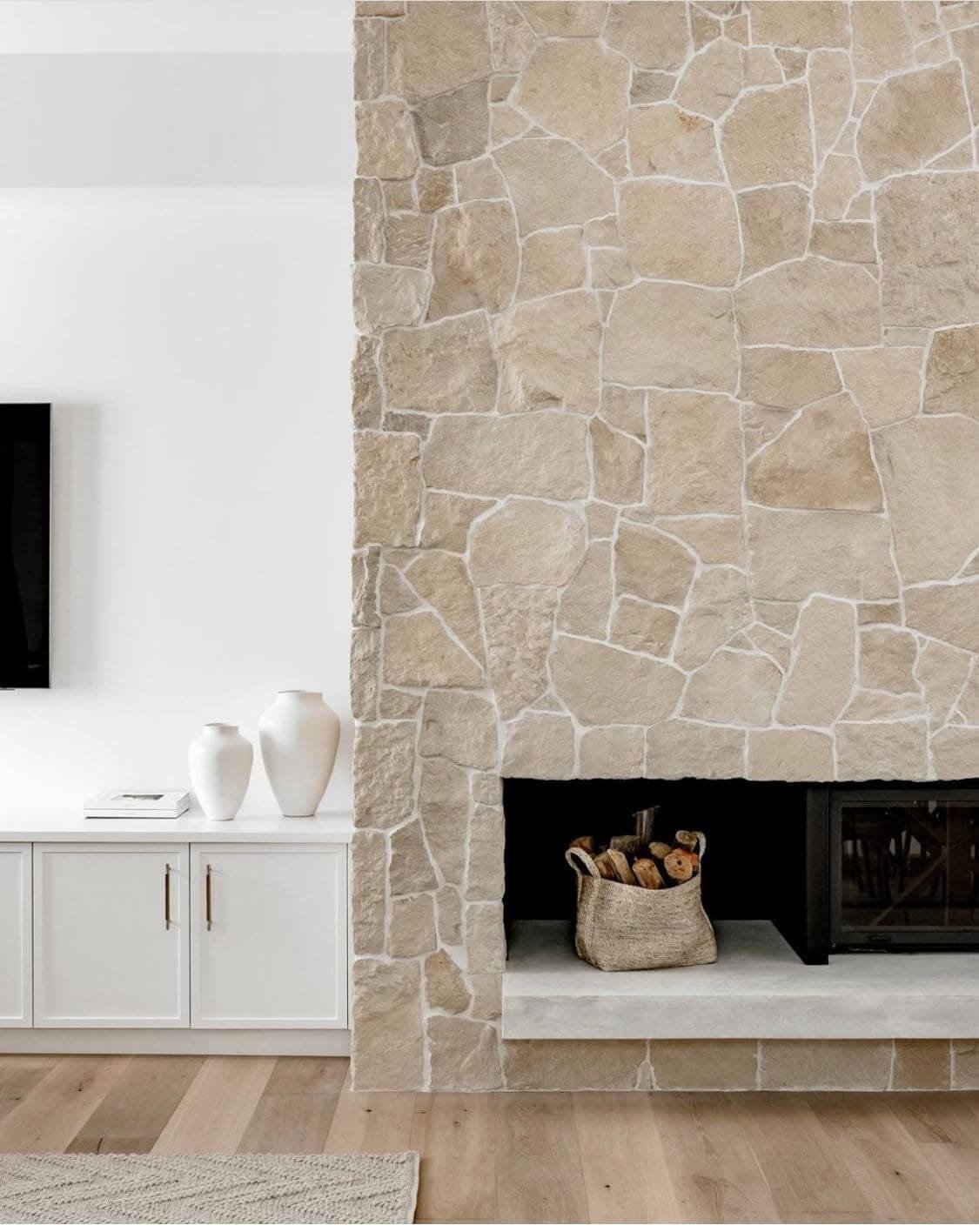 a cream stone fireplace with white grout and a TV over cabinets in living room